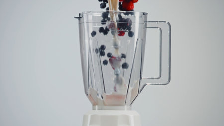 Streams of milk, raspberries, blackberries, blueberries and blackcurrants pour into the transparent blender flask.の写真素材