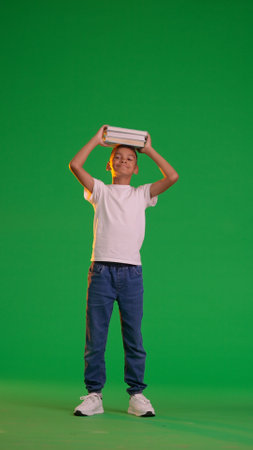 Happy Schoolboy Balancing Books on Head Against Green Screenの写真素材