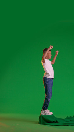 Joyful Schoolboy Celebrating on Green-Covered Box Against Green Screen