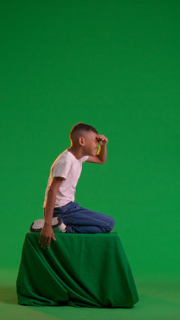A schoolboy gazes into the distance, covering his eyes with his hand, at the green screenの写真素材