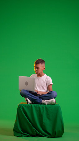 Young Boy Focused on Using Laptop While Sitting Against on a green screenの写真素材