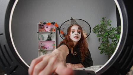 Young woman beauty blogger in witch costume at home films video tutorial for halloween party makeup on smartphone.の写真素材