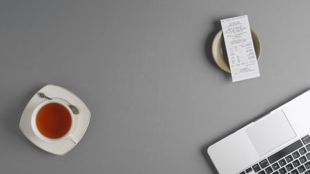 Top view of a table in a cafe or restaurant with a check resting on a saucer. Next to it are a cup of tea and a laptop. Freelance work in a cafe, remote learning.の写真素材