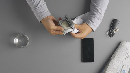 Top view of man counting wad of US dollars money banknotes in envelope and leaving it on the table.