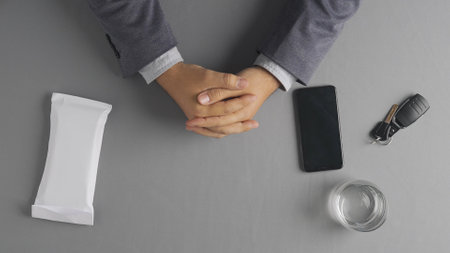 Top view of a man sitting at a table. An envelope with money, car keys, a smartphone and a glass of...