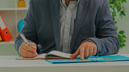 A man in a suit sits in an office and writes down the name of countries in a notebook.の写真素材