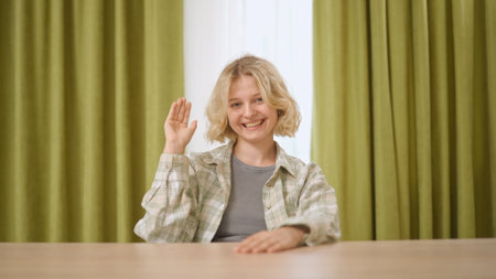 Female college student studying at home, listening watching lesson online on computer, raises hand answering question. Modern online education.の写真素材