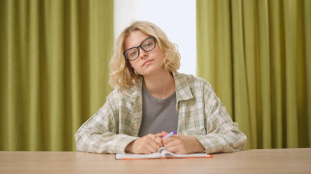 Female college student studying at home, sitting at desk listening watching lesson online on computer, writing in notebook. Modern online education.の写真素材