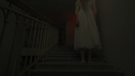 Creepy ghost woman in white dress alone dead walking down the staircase in dark haunted house, glitch video effect. Halloween horror advertisement concept.の写真素材