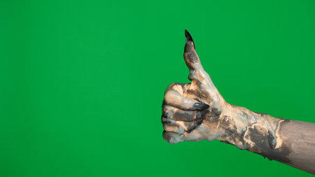 Creepy halloween monster hand in black paint with nails shows thumb up good sign, isolated on chroma key green screen background, workspace mockup.の写真素材