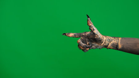 Creepy halloween monster hand in black paint with nails moving pointing finger at side, isolated on chroma key green screen background, workspace mockup.の写真素材