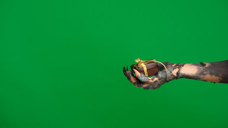 Creepy halloween monster hand in black paint with nails holding gift box with ribbon, isolated on chroma key green screen background, workspace mockup.の写真素材