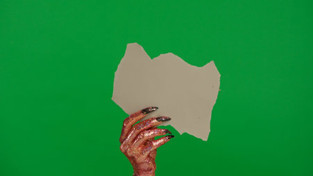 Creepy halloween monster human hand in glitter slime with nails holds empty ripped paper sign, isolated on chroma key green screen background, workspace mockup.の写真素材