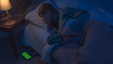 Woman sleeping in bed in apartment room, monster hiding under bed. Scary hand with smartphone chroma key green screen crawls out. Halloween horror concept.の写真素材