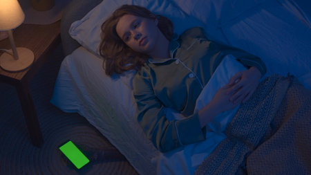 Woman sleeping in bed in apartment room, monster hiding under bed. Scary hand with smartphone chroma...