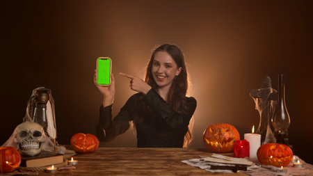 Halloween gothic woman witch fortune teller sitting at table holds smartphone chroma key green...