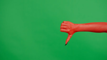 Creepy halloween devil monster hand in red paint with black nails shows bad thumb down sign, isolated on chroma key green screen background, workspace mockup.の写真素材