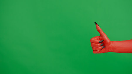 Creepy halloween devil monster hand in red paint with black nails shows like thumb up sign, isolated on chroma key green screen background, workspace mockup.の写真素材