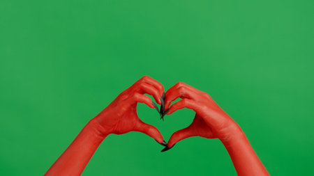 Creepy halloween devil monster hand in red paint with black nails shows hand heart sign, isolated on chroma key green screen background, workspace mockup.の写真素材