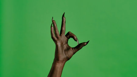 Creepy halloween devil monster hand in black paint with nails shows ok finger sign, isolated on chroma key green screen background, workspace mockup.の写真素材