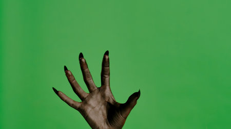 Creepy halloween monster hand in black paint with nails shows crawling catching, isolated on chroma key green screen background, workspace mockup.の写真素材