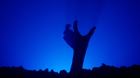 Scary dirty halloween zombie hand silhouette raising up from grave crawling and moving fingers, isolated on blue background. Mystery halloween concept.の写真素材