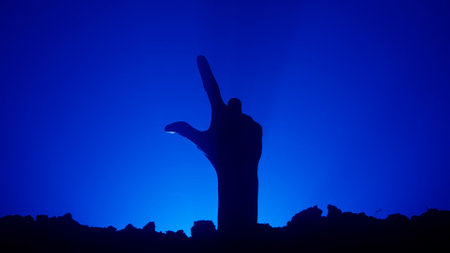 Scary dirty halloween zombie hand silhouette raising up from grave pointing finger up, isolated on blue background. Mystery halloween concept.の写真素材