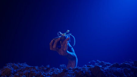 Scary dirty halloween zombie hand raising up from grave ground, holding small gift box, isolated on blue background. Mystery halloween concept.の写真素材