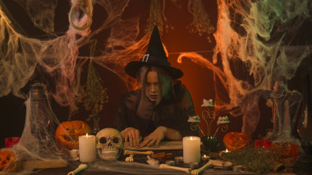 A witch in black clothing conjures over a Ouija board while sitting in a spooky kitchen with...