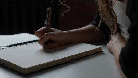 Woman sitting at desk and writing, taking notes in notebook on sheets with pencil, concentrated person writing down notes and ideas, close up shot of handwriting.の写真素材