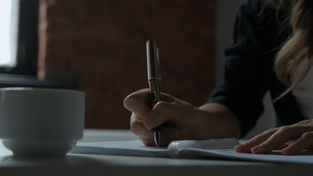 Business woman sitting at office desk writing taking notes in notebook with pen, concentrated person writing down ideas and planning events, close up shot.の写真素材