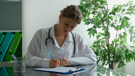 Woman doctor in white coat sitting at desk writing application, filling patient medical rx form documents on clipboard. Medical treatment concept.の写真素材