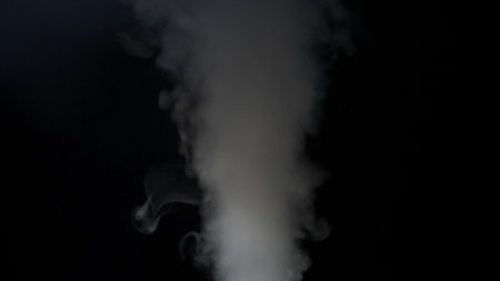 Close-up of white smoke clouds against a black background. Contrast of brightly lit smoke and dark room. Cinematographic light.の写真素材