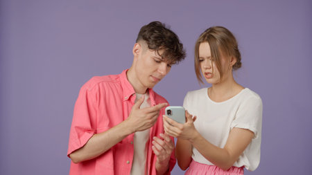 Positive couple of young boyfriend and girlfriend in pink white clothes scroll social media on smartphone, talk and watch content, isolated on purple background.の写真素材