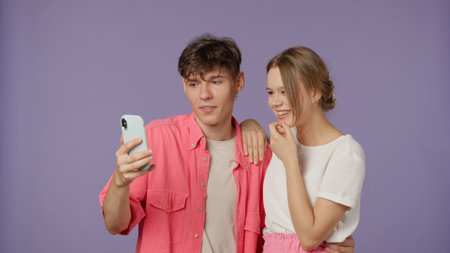Positive couple of young boyfriend and girlfriend in pink white clothes isolated on purple...