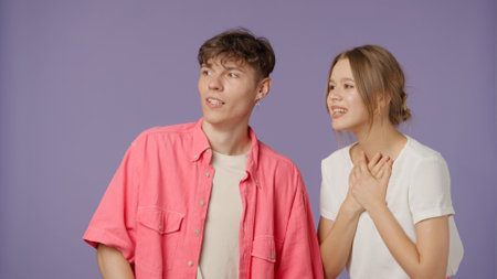 Positive couple of young boyfriend and girlfriend in pink white clothes isolated on purple background, girl looks surprised with wow amazed expression.の写真素材
