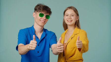 Positive couple of young boyfriend and girlfriend in yellow blue clothes isolated on green background look at camera smiling expression showing thumbs up.の写真素材