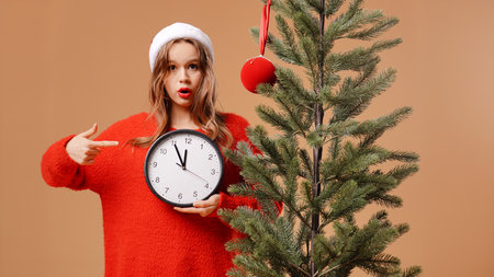 Young girl in red sweater and a New Years hat poses in the studio on a beige background