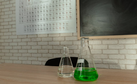 Empty elementary school chemistry classroom with chalkboard, workspace for studying. Teachers desk with glass bottle, periodic table on the wall, close up.の写真素材