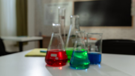 Empty school chemistry classroom with desks, chairs and chalkboard, workspace for teaching and studying. Glass bottles with colorful liquids close up.の写真素材