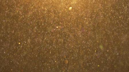 Many sparkling glitters showering floating in light on empty golden background with light from above.の写真素材
