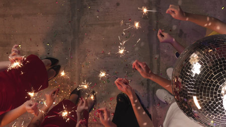 Teenagers birthday party, girls and boys stand in circle and lightning up many sparkles bengal lights together, top view shot. Happy group of young people having fun together.の写真素材