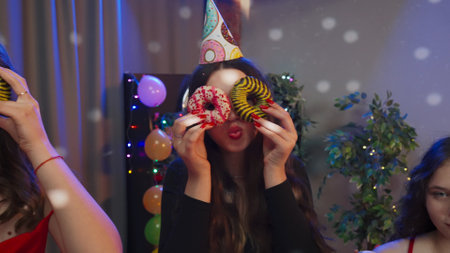 Teenagers birthday party, girls in festive outfits posing at camera making funny faces with donuts,...