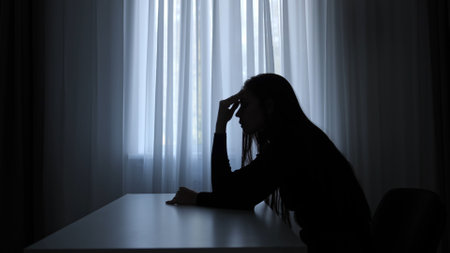 Silhouette of woman sitting at table in front of window, disappointed depressed expression, mental crisis, exhausted frustrated mood. Human emotions and mental health.の写真素材