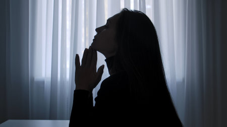 Silhouette of woman sitting at table in front of window, thinking feels stress indecisive, depressed exhausted expression.. Human emotions and mental health.の写真素材
