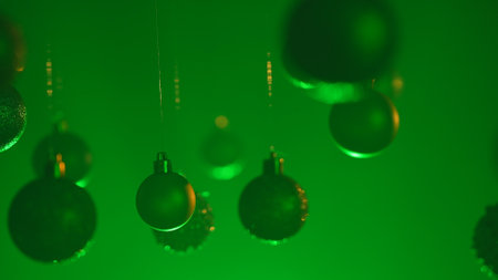Christmas tree golden silver balls highlighted by green neon light hanging from above, glittering ornaments garland close shot on blurred festive background.の写真素材