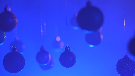 Christmas tree golden silver balls highlighted by blue neon light hanging from above, glittering ornaments garland close shot on blurred festive background.の写真素材