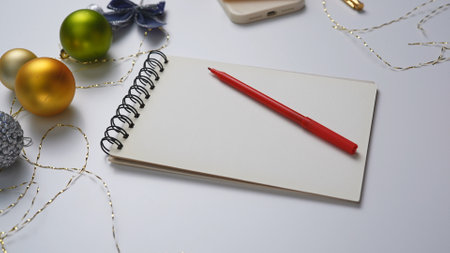 Close up shot of christmas decorated white table, notebook with empty blank page and pen laying on...