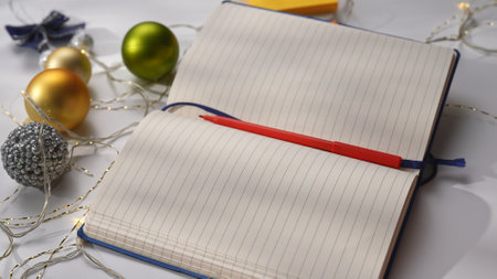 Close up shot of christmas decorated white table, open notebook with empty blank page and pen laying...