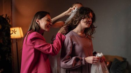 Group of young women friends and bride celebrating bachelorette party at home, waiting for bride, girls putting on the brides veils in front of the mirror and posing.の写真素材